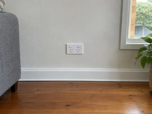 Double power point on a painted wall above white skirting in a living room with timber floor in Brookvale