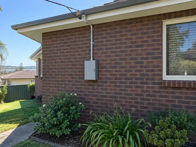 Overhead service cable and point-of-attachment bracket on a brick house exterior in Dee Why