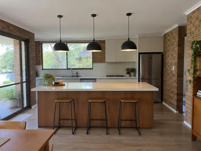 Three black pendant lights above a kitchen island in a brick-walled home in Narrabeen