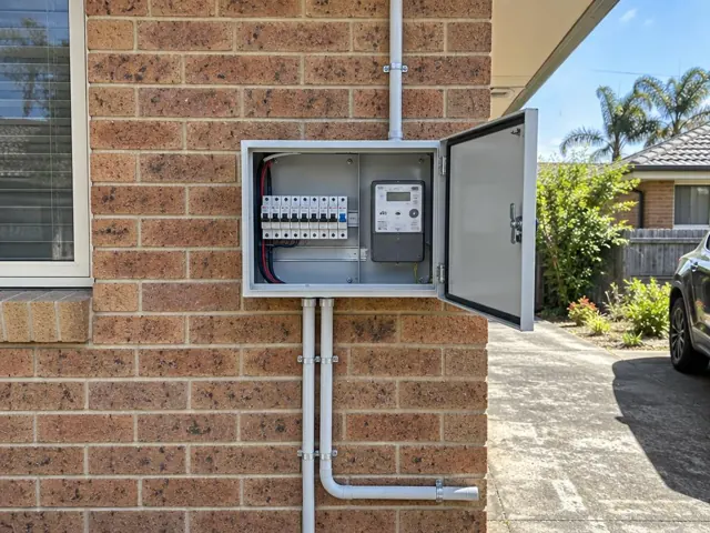 Open external switchboard on a brick house wall beside conduit and meter box in Cromer